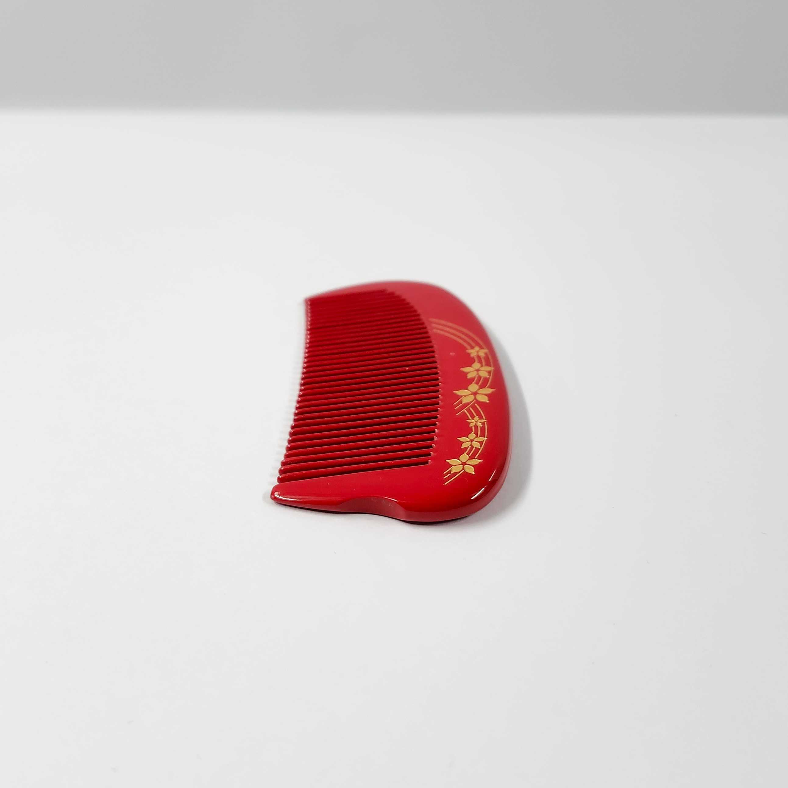 This is another side view of the comb. There's a simple graphic on the front side of the comb that illustrates lines and flowers. It's slightly carved into the comb with gold ink. From this side the comb curves inwards in the middle, and the thickness gets thinner towards the end. 